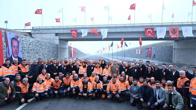 Yolda toplanmış kalabalık, arka planda Türk bayrakları ve bir köprü görünmekte.