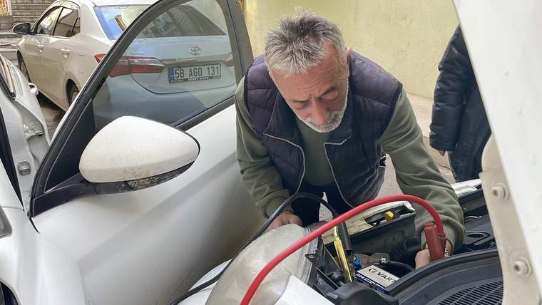 Bir kişi, açık kaputun altındaki otomobil aküsüne kırmızı ve siyah takviye kabloları bağlıyor.