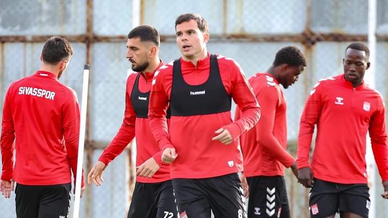 Kırmızı antrenman formaları giyen futbolcular, sahada yan yana koşu çalışması yapıyor.