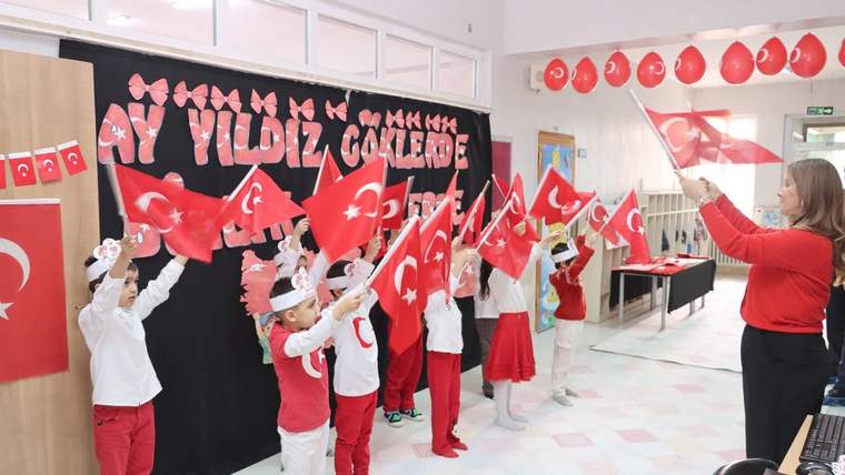 Kırmızı ve beyaz kıyafetler giymiş çocuklar, Türk bayrağı sallayarak bir etkinlikte yer alıyor.