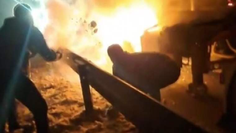 Alevler içinde bir tır ve kar atan birkaç kişi, yangına müdahale ediyor.