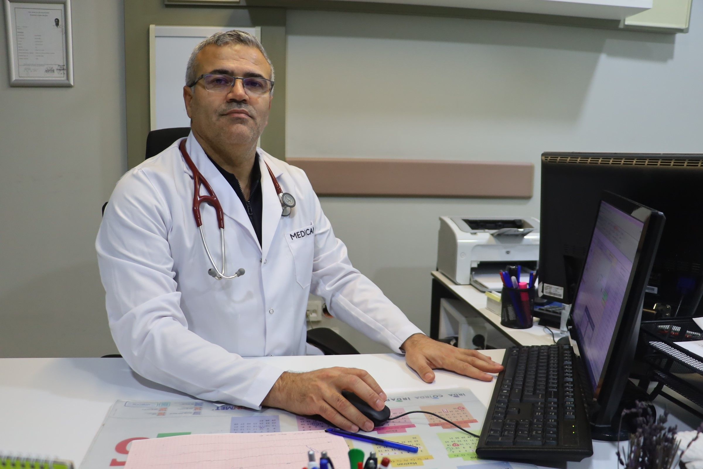 Beyaz önlük giymiş bir doktor, bilgisayarın önünde oturuyor.