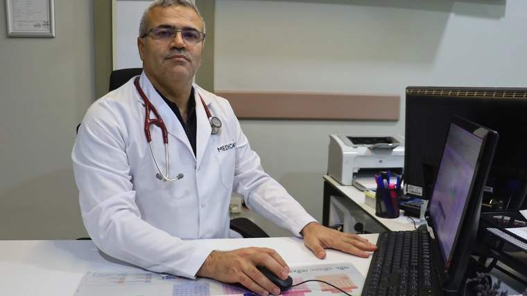 Beyaz önlük giymiş bir doktor, bilgisayarın önünde oturuyor.