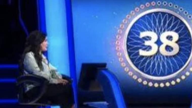 Televizyon stüdyosunda oturan bir kişi, yanında büyük “38” sayısının yer aldığı mavi dekorun önünde görülüyor.