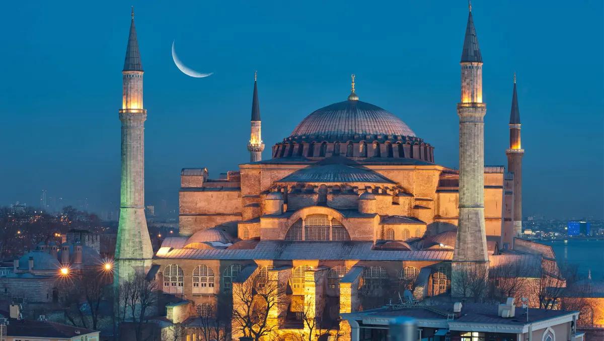 Ayasofya, akşam saatlerinde aydınlatılmış olarak görünmekte, arka planda hilal yer almakta.