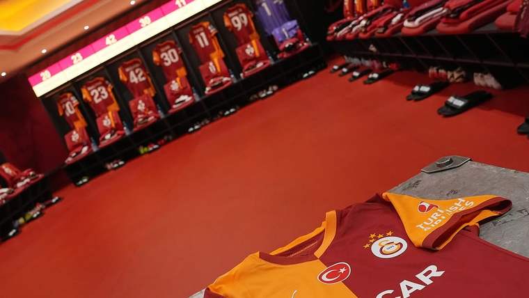 Kırmızı zeminli soyunma odasında askılarda formalar, önde Galatasaray armalı turuncu-kırmızı forma görülüyor.