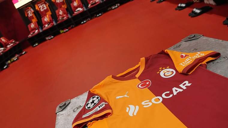 Kırmızı zeminli soyunma odasında askılarda formalar, önde Galatasaray armalı turuncu-kırmızı forma görülüyor.