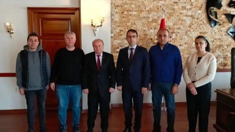 Ahşap kapı ve taş duvar önünde, aralarında fes takan bir kişinin bulunduğu altı kişi yan yana duruyor.