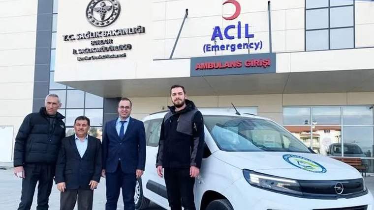 Hastane acil girişinin önünde dört erkek ve üzerinde sağlık amblemi bulunan beyaz ambulans duruyor.