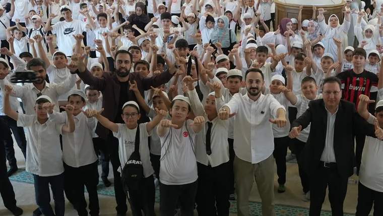 Ayyıldız Camii'nde toplanmış, beyaz tişörtlü ve şapkalı kalabalık bir grup öğrenci, ellerini havaya kaldırmış.
