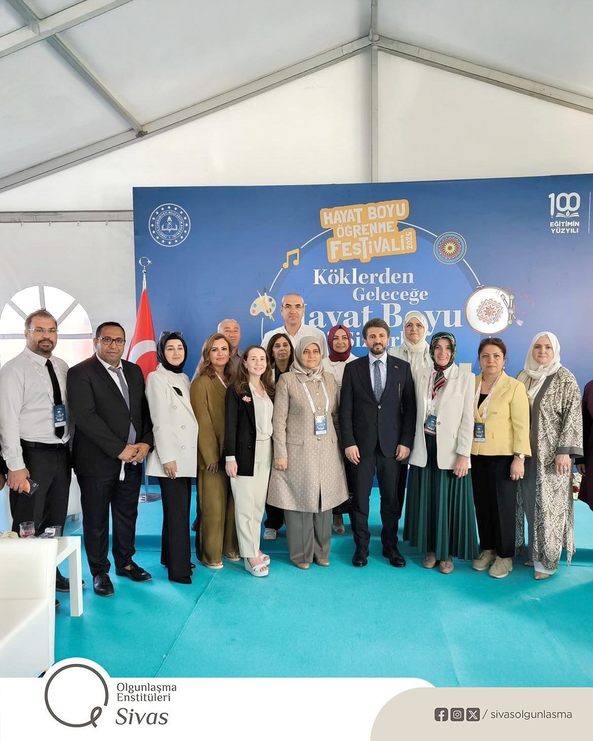 Üzerinde Hayat Boyu Öğrenme Festivali yazan pano önünde, farklı yaşlardan 13 kişi birlikte duruyor.