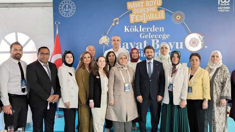 Üzerinde Hayat Boyu Öğrenme Festivali yazan pano önünde, farklı yaşlardan 13 kişi birlikte duruyor.
