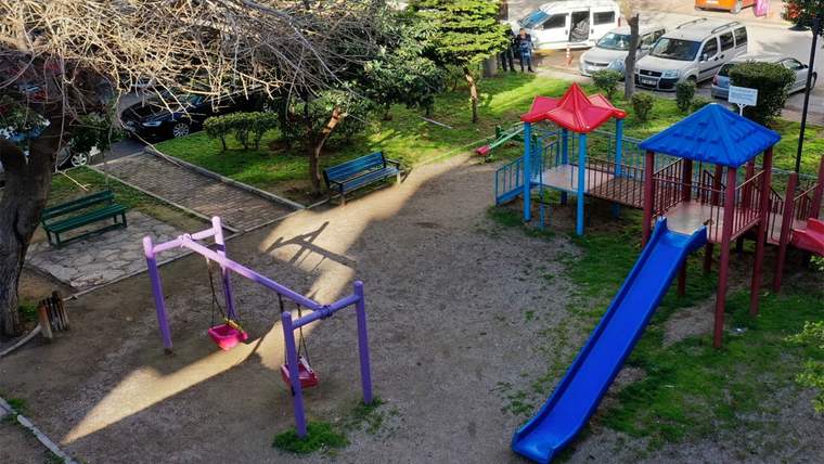 Boş bir çocuk parkında salıncak, kaydırak ve banklar görünmekte.