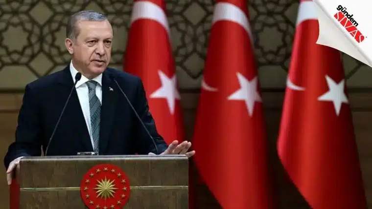 Bir kişi, arkasında Türk bayrakları ile bir kürsüde konuşuyor.