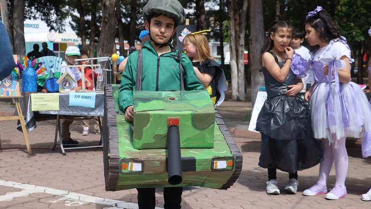 Yeşil askeri kıyafet giymiş bir çocuk, kartondan yapılmış tank kostümüyle duruyor.