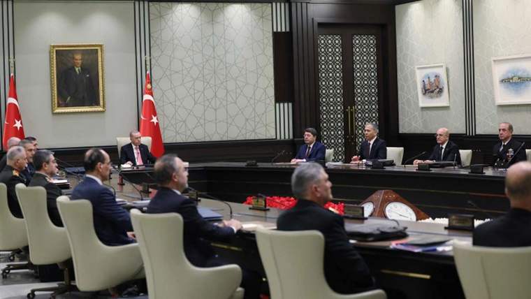 Toplantı masasında oturan kişiler, arka planda Türk bayrağı ve bir tablo var.