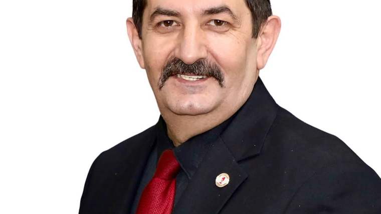 Bıyıklı bir erkek, siyah takım elbise ve kırmızı kravatla beyaz arka plan önünde görülüyor.