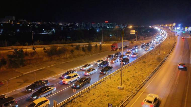 Gece çekiminde çok sayıda otomobil ve bir kamyon, bölünmüş yolda yoğun trafikte ilerliyor.