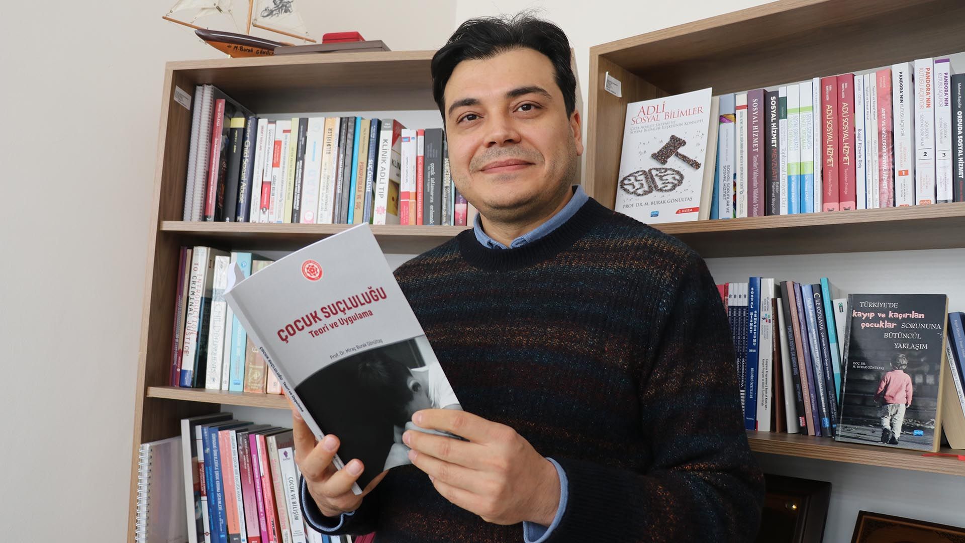 Kitaplık önünde duran bir kişi, üzerinde “Çocuk Suçluluğu” yazan kitabı iki eliyle tutuyor.