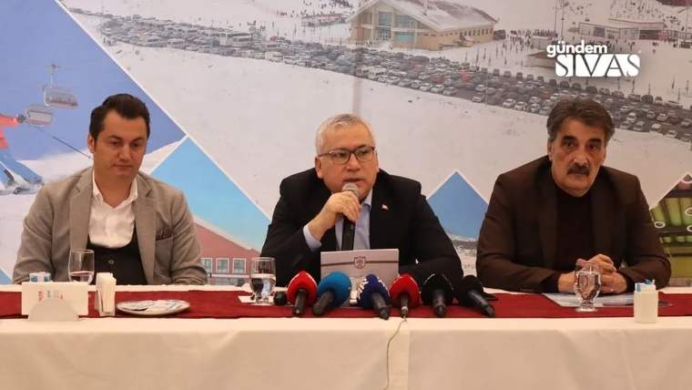 Masada oturan üç kişiden ortadaki mikrofonla konuşurken, önlerinde çok sayıda mikrofon bulunuyor.