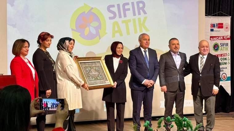 Sahnede, üzerinde “SIFIR ATIK” yazılı ekran önünde duran altı kişi, çerçeveli bir çalışmayı birlikte tutuyor.