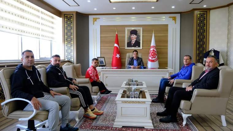 Makam odasında bir masanın çevresinde oturan altı kişi, Türk bayrağı ve iki flamanın önünde görülüyor.