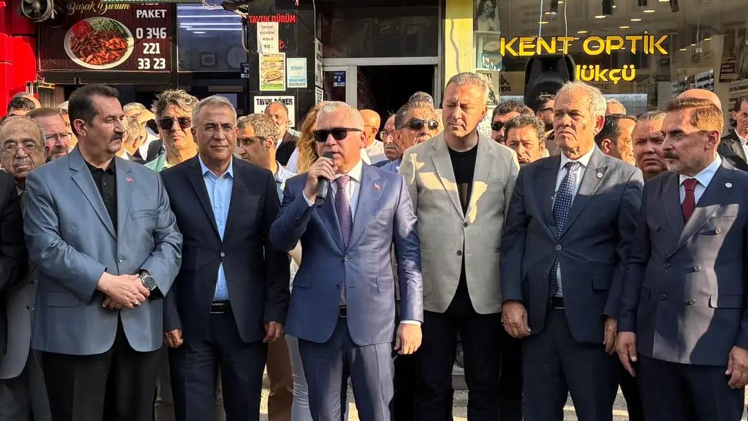Bir grup erkek, yeni hizmet binası açılışında konuşma yapan bir kişiyi dinliyor.
