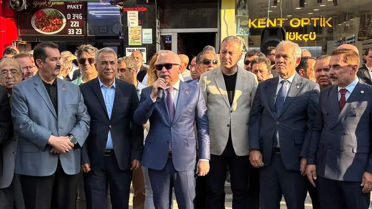 Bir grup erkek, yeni hizmet binası açılışında konuşma yapan bir kişiyi dinliyor.