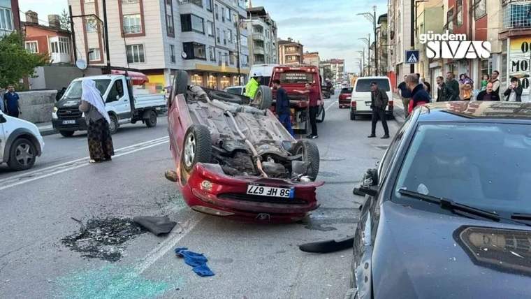 Ters dönen kırmızı bir otomobil, sokakta yan yatmış halde duruyor.