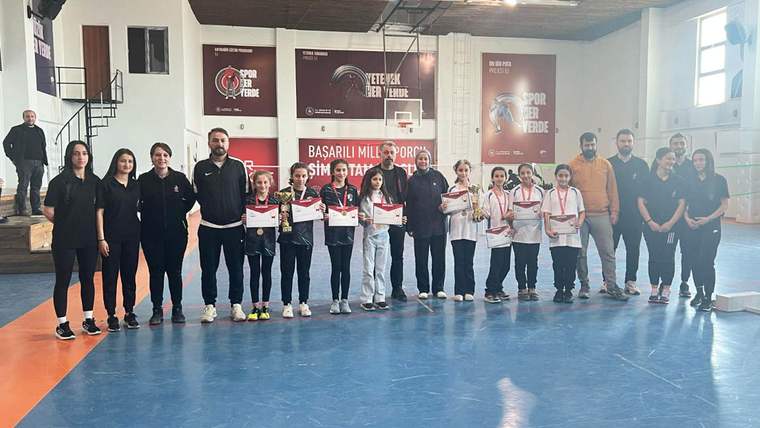 Spor salonunda madalya ve sertifika taşıyan çocuklar, yetişkinlerle birlikte yan yana duruyor.