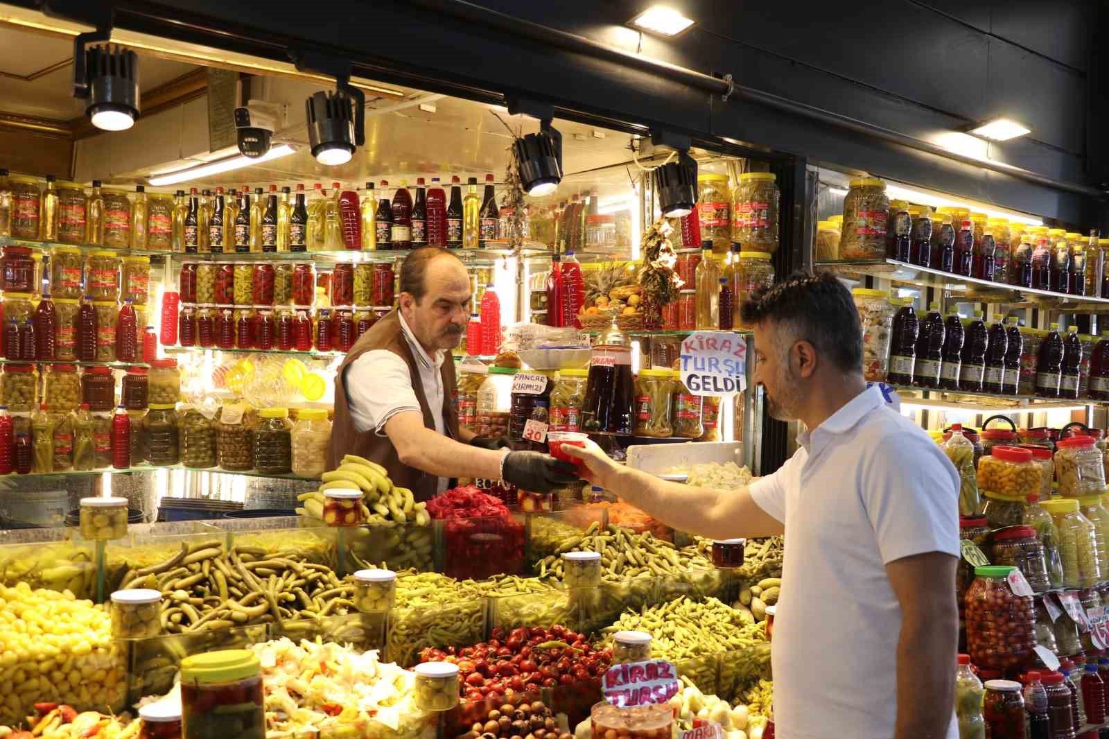 Turşu tezgâhında kavanozlar ve mısır koçanları sergilenirken iki kişi alışveriş yapıyor.
