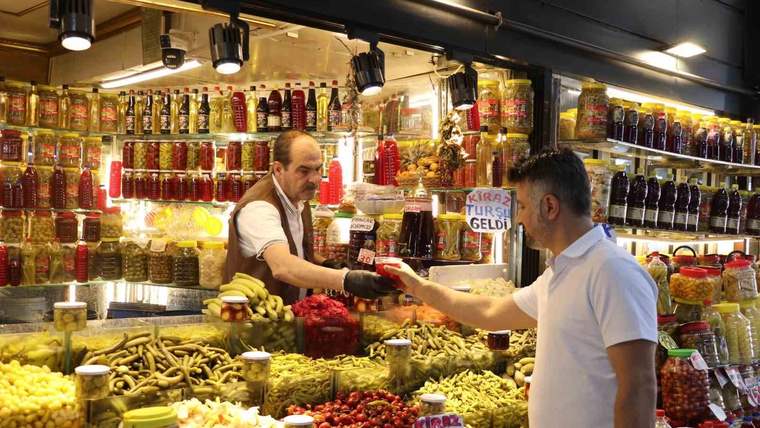 Turşu tezgâhında kavanozlar ve mısır koçanları sergilenirken iki kişi alışveriş yapıyor.