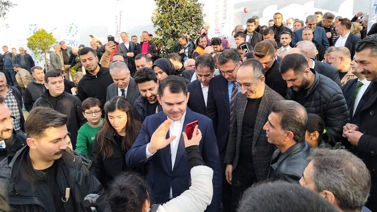 Bir grup insan, bir erkeğin etrafında toplanmış, bazıları telefonla fotoğraf çekiyor.