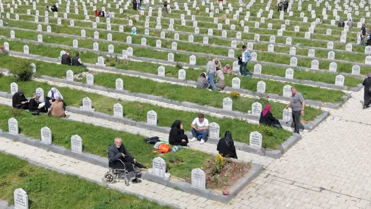Bir mezarlıkta, mezarların arasında oturan ve dua eden insanlar görünüyor.