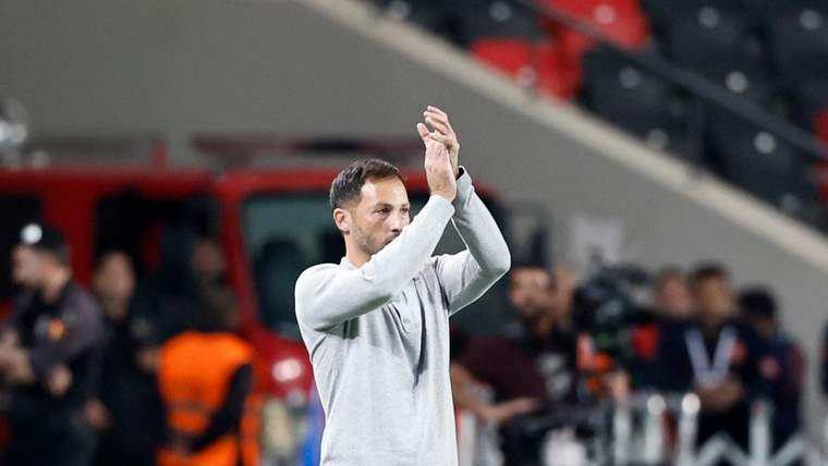 Futbol sahasının kenarında duran bir kişi, ellerini baş hizasında birleştirerek alkışlıyor.