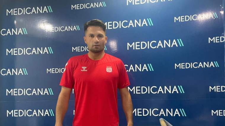 Kırmızı spor tişörtlü bir kişi, Medicana yazılı panonun önünde egzersiz cihazının yanında duruyor.