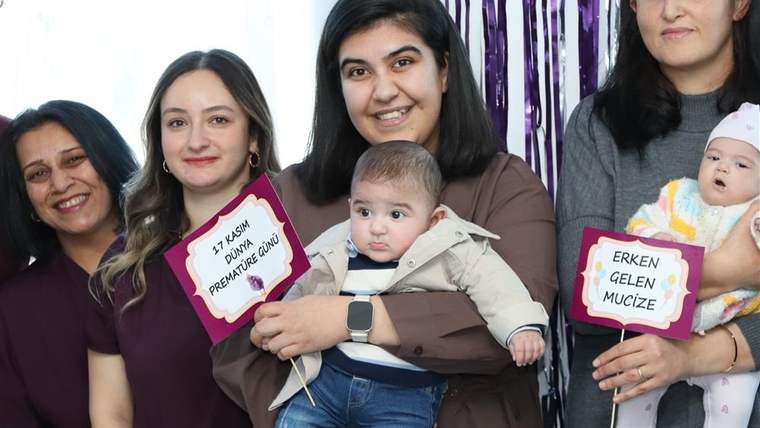 Prematüre günü etkinliğinde bir kadın, kucağında bir bebek tutuyor; diğer kadınlar da yanlarında duruyor.