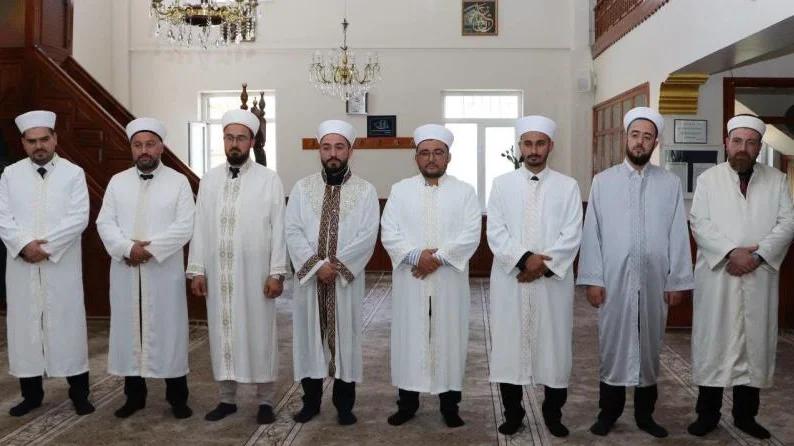 Beyaz giysili sekiz kişi, bir cami içinde yan yana duruyor.