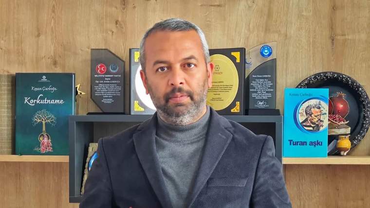 Bir adam, arkasında ödüller ve kitaplarla birlikte kameraya bakıyor.