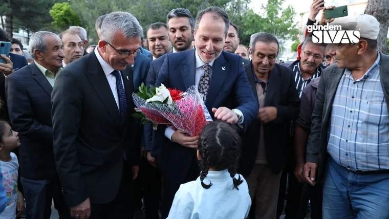 Takım elbiseli bir grup erkek, ellerinde çiçek buketi bulunan bir adam ve karşısındaki çocukla birlikte duruyor.