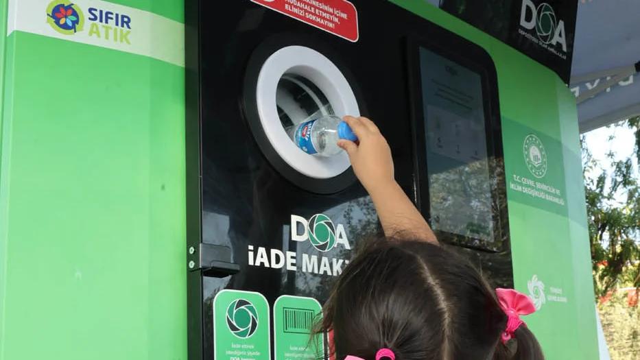Bir çocuk, geri dönüşüm için su şişesini iade makinesine atıyor.