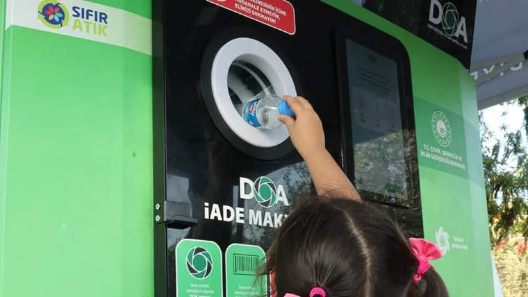 Bir çocuk, geri dönüşüm için su şişesini iade makinesine atıyor.