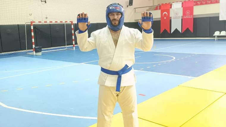 Mavi kuşaklı bir sporcu, karate giysisiyle poz veriyor.