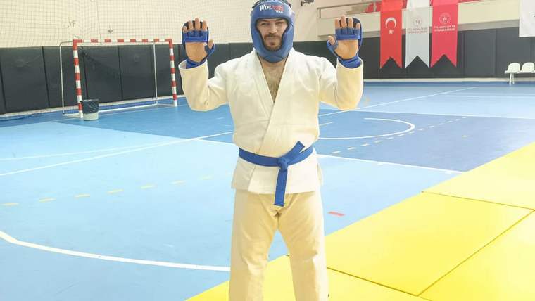 Mavi kuşaklı bir sporcu, karate giysisiyle poz veriyor.