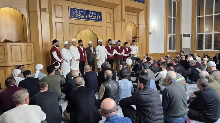 Camide, teravih namazı için toplanmış kalabalık bir grup insan, sahneye bakan bir dizi kişiyle birlikte oturuyor.