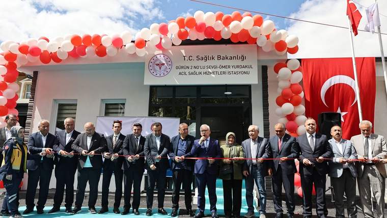 Balonlarla süslenen acil sağlık hizmetleri istasyonu önünde, kurdele kesen bir grup insan görülüyor.