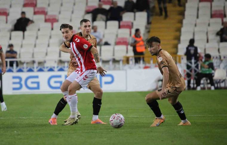 Futbol sahasında kırmızı-beyaz formalı oyuncu topa ilerlerken iki kahverengi formalı oyuncu onu takip ediyor.