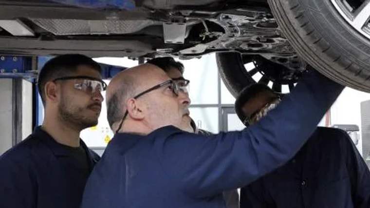 Bir grup öğrenci, bir öğretmenin yönlendirmesiyle otomobilin alt kısmını inceliyor.