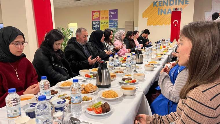 Uzun bir masa etrafında oturan insanlar, yemek ve içeceklerle dolu tabaklar önünde dua ediyor.
