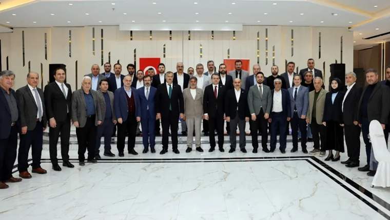 Geniş bir salonda, arkasında Türk bayrağı bulunan kalabalık bir grup birlikte ayakta poz veriyor.